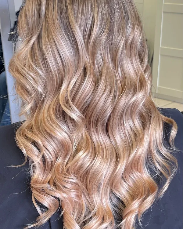 Back view of long curled hair with rooted balayage fading into warm caramel-blonde ends